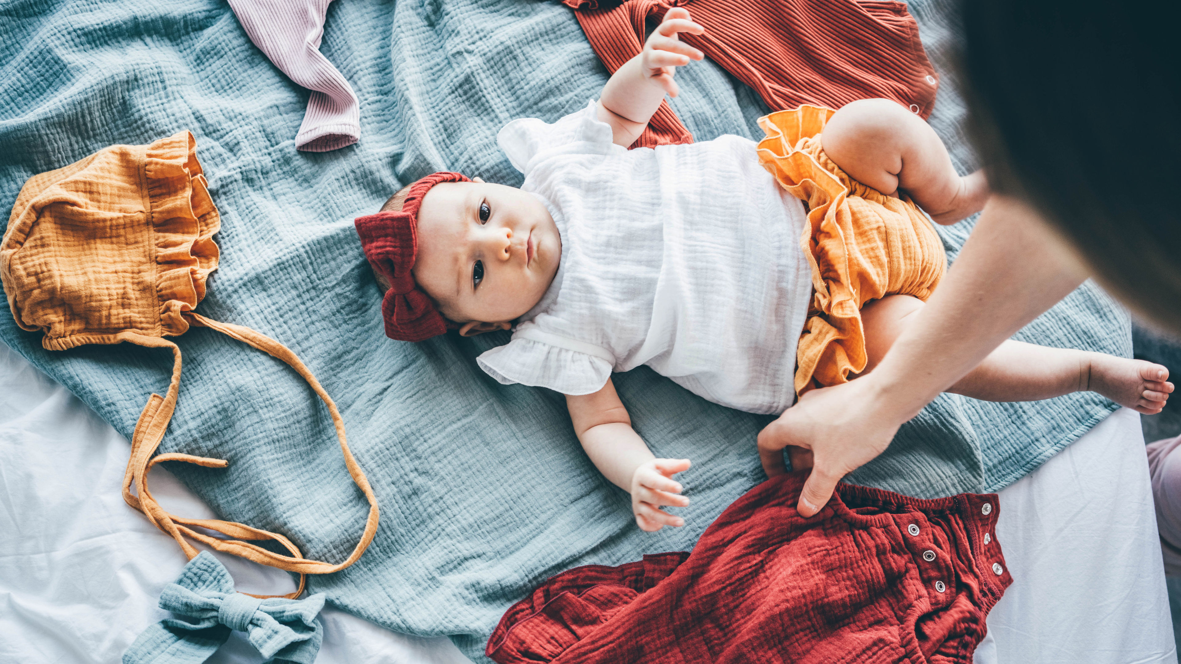 A baby lying on bed surrounded with dress