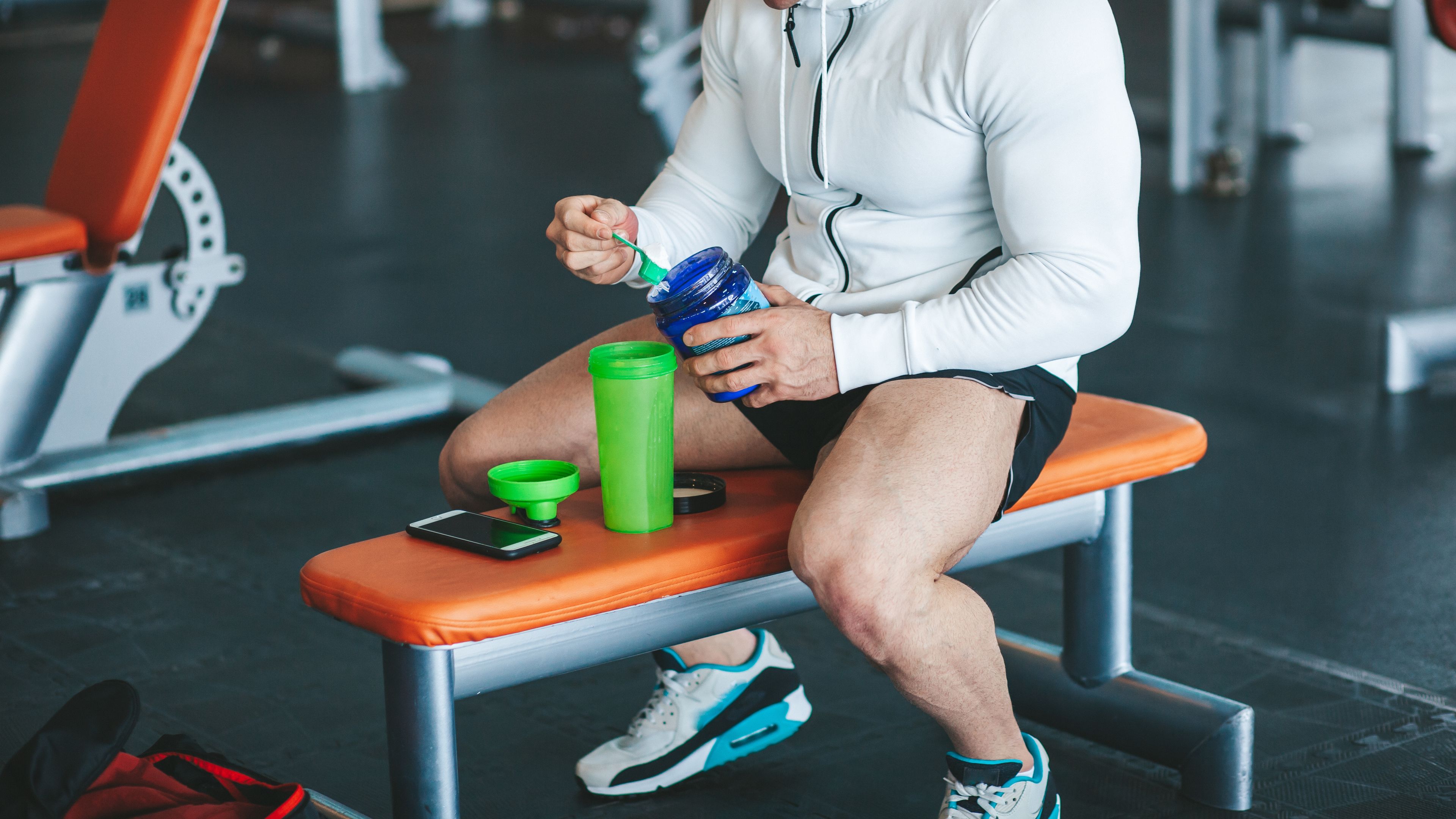 Athletic male body builder scooping up protein powder in gym