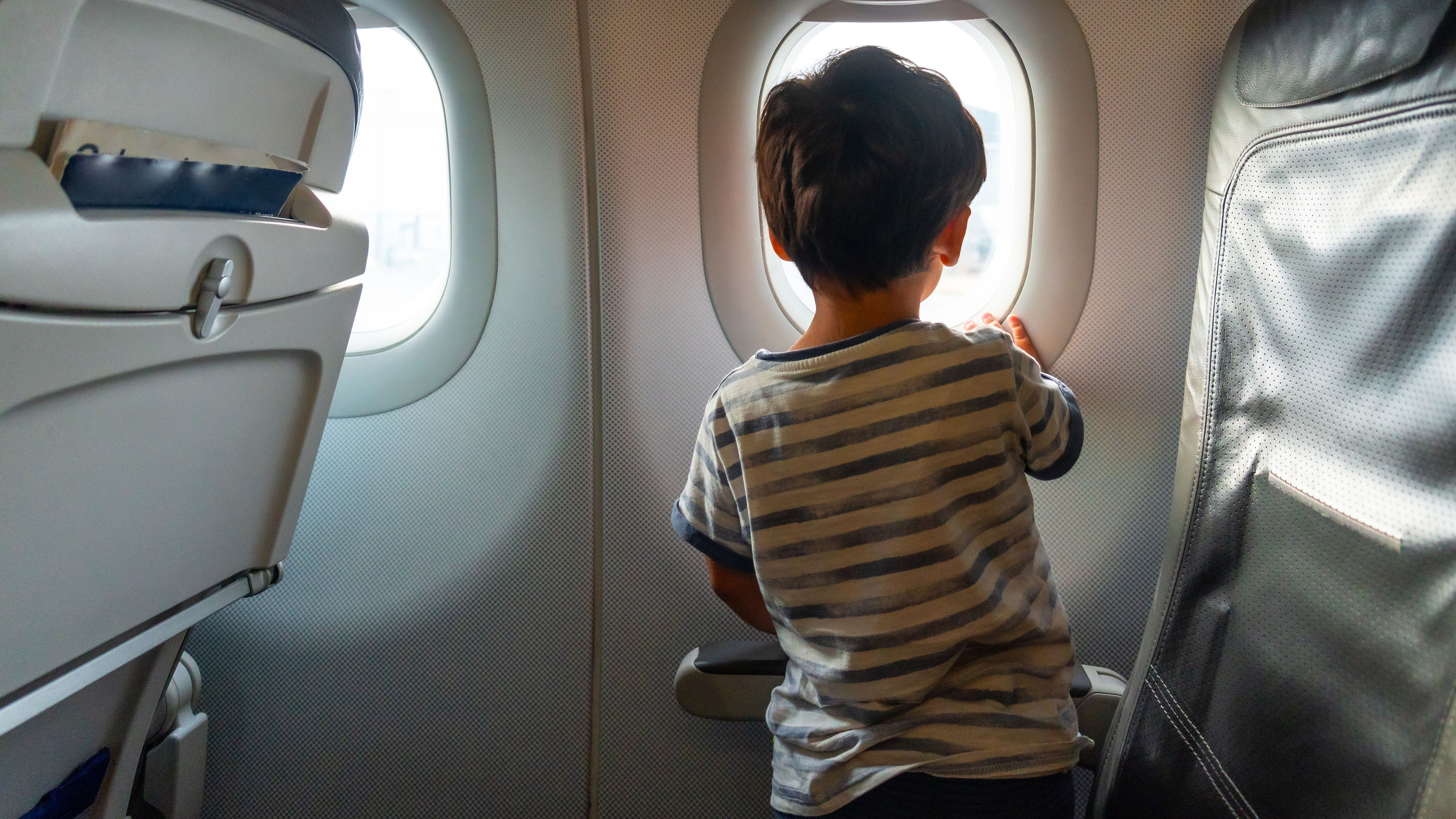 Child in the looking out the airplane window traveling on summer vacation.