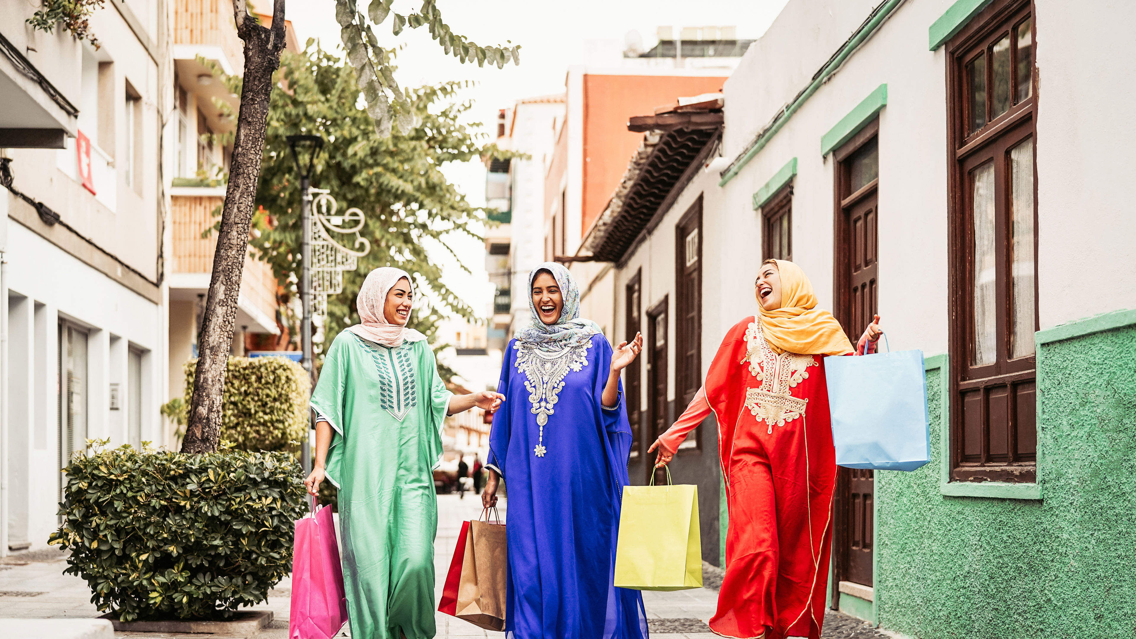 Three friends in vibrant abayas enjoying a joyful shopping day.